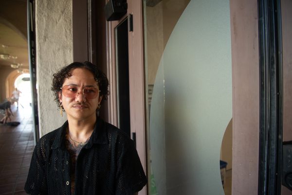 A person with sunglasses and a black shirt stands in front of a glass door