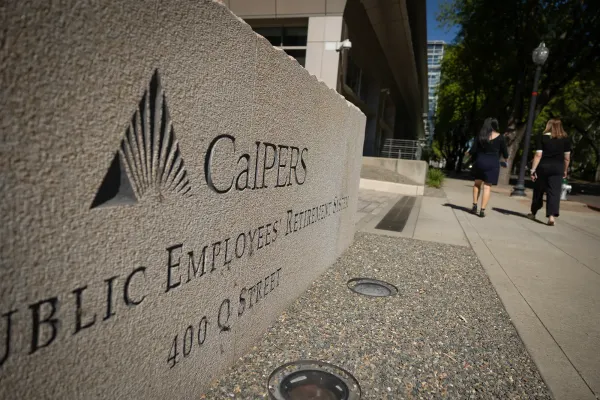 Concrete sign that says CalPERS with people wearing black walking away from the camera next to it
