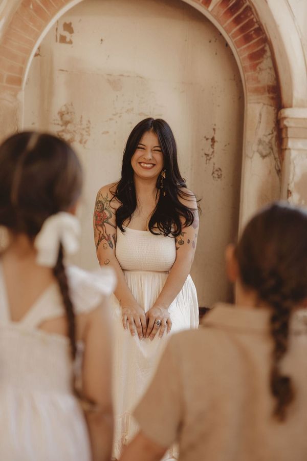 Picture of a woman in a white dress with two kids in front of her with their backs to the camera