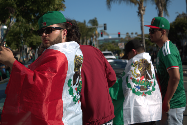 People wearing baseball caps and jerseys with red, white and green and with Mexican flags draped across their shoulders