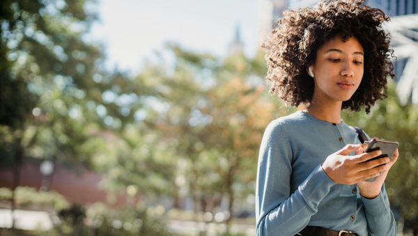 Picture of a teenage on a cell phone in front of trees and buildings blurred in the background