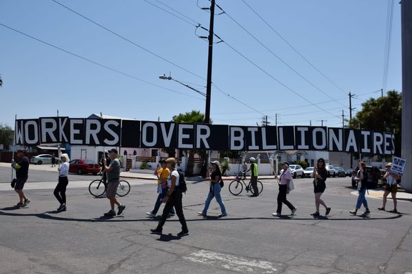 People hold a black sign with white letters that says workers over billionaires