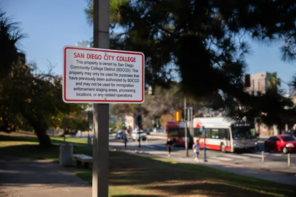A sign with red and black text in front of a street and lawn area