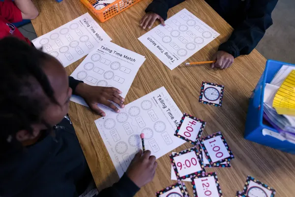 Students work on a telling time worksheet at a table