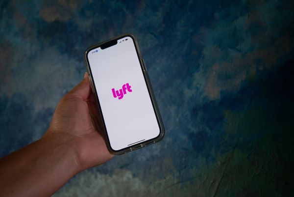 A hand holds a cellphone with the words lyft written in pink on it and a blue background