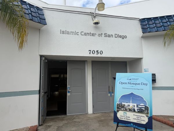 A white building with the sign Islamic Center of San Diego over the gray doors and a blue sign on an easel that says Open Mosque Day