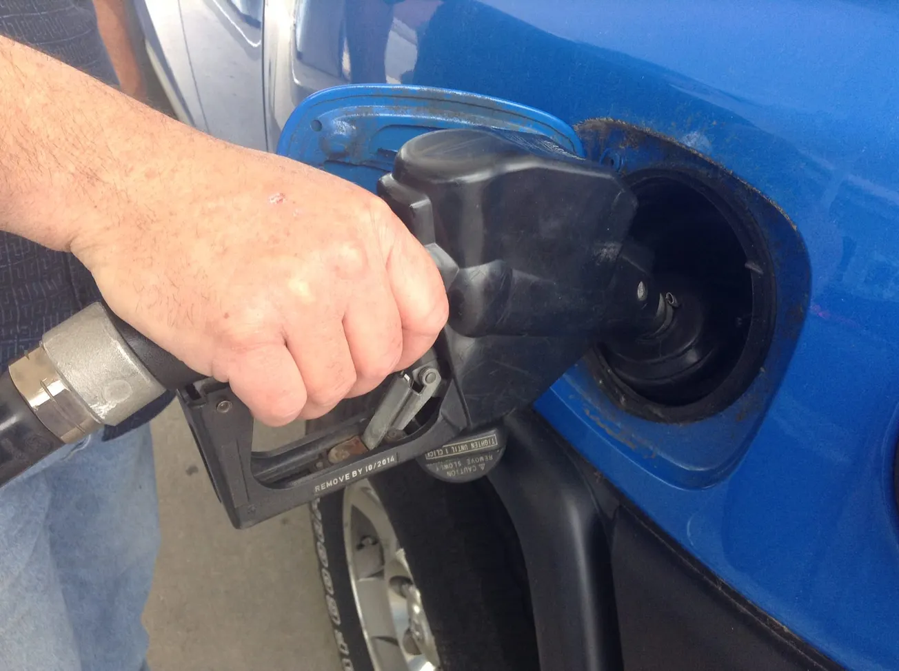 A man pumps gas into a blue car.