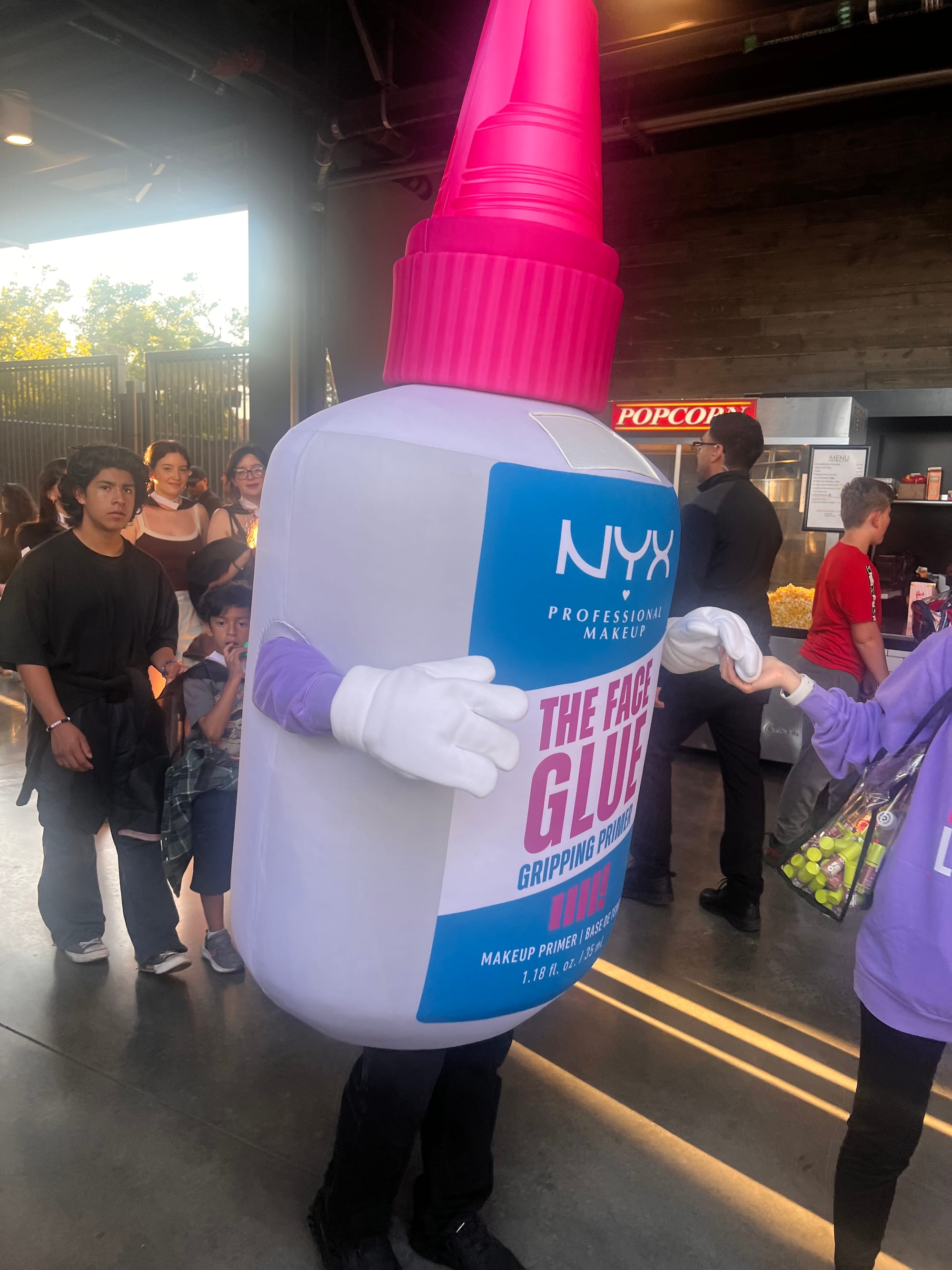 a nyx makeup "the face glue gripping primer" mascot. it is shaped like a glue bottle but it has arms and hands with three fingers and legs and feet.
