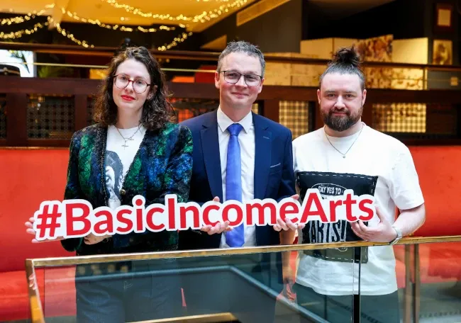 Le ministre O’Donovan et deux membres de son équipe tiennent dans leurs mains un hashtag en 3D : #BasicIncomeArts.