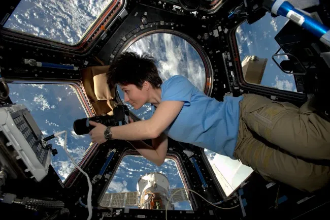Une astronaute flottant dans la coupole de la station spatiale internationale. Derrière elle, en arrière-plan : la Terre.