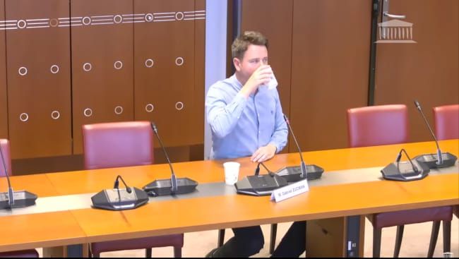 Lors de son audition àl'Assmblée Nationale, Gabriel zucman, en chemise bleue bien boutonnée, boit un verre d'eau.