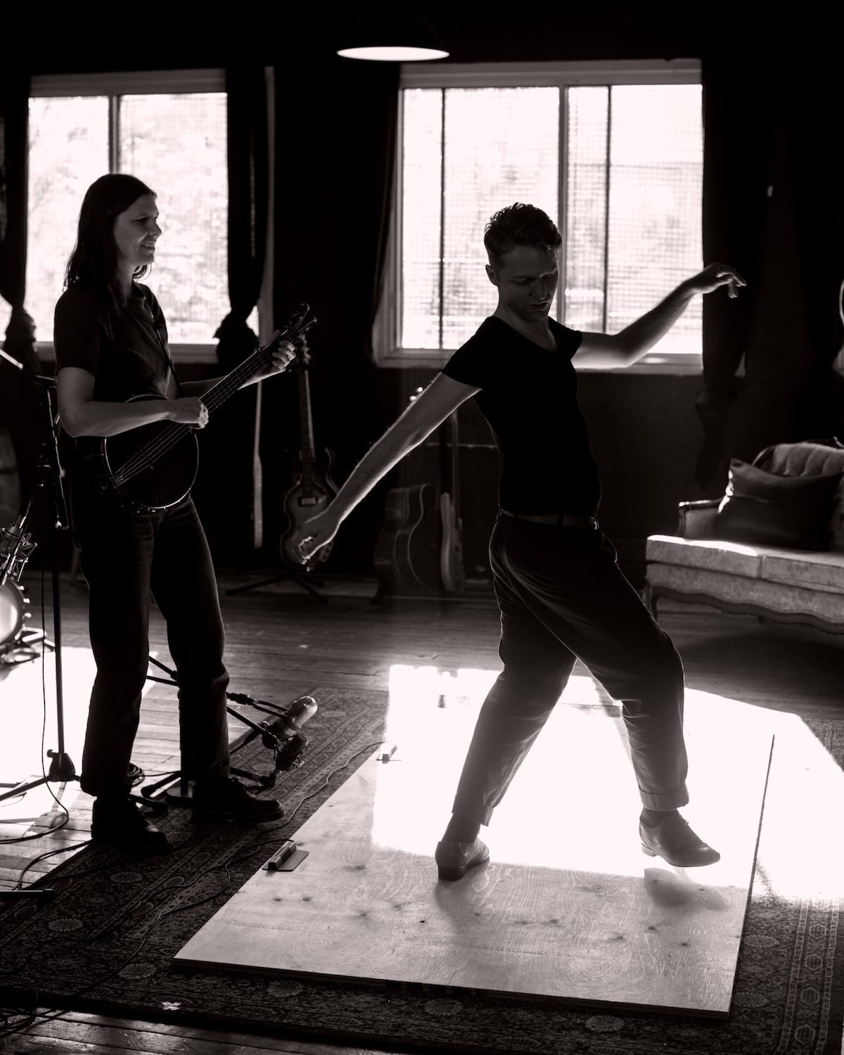 Allison de Groot plays banjo while Nic Gareiss dances on a wooden plank