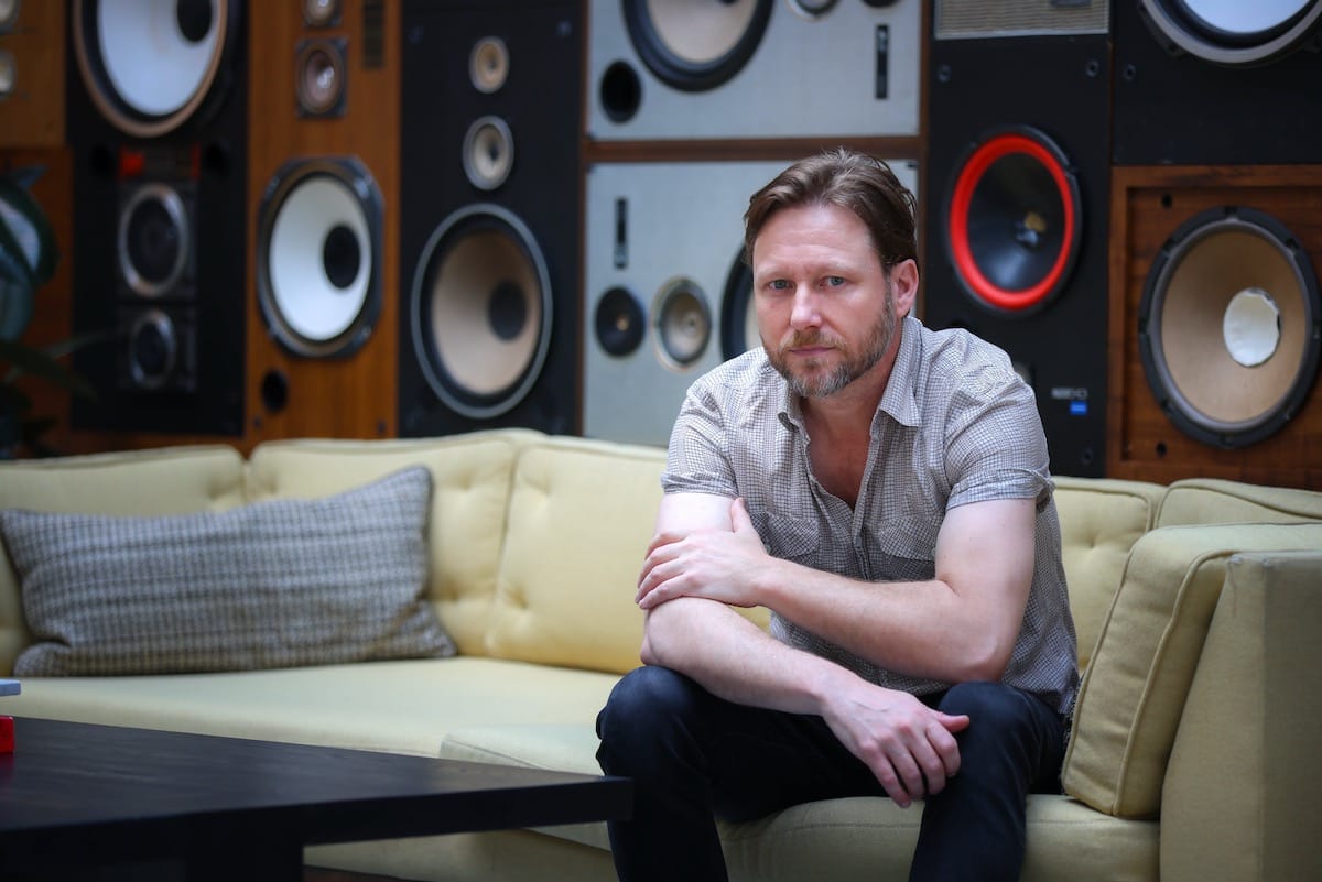 Cory Branan on a yellow couch with speakers in the background