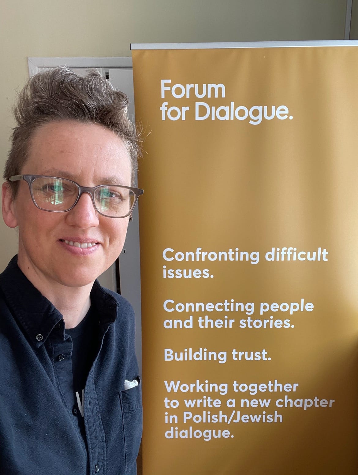 Ana Egge next to an amber sign for the Forum for Dialogue