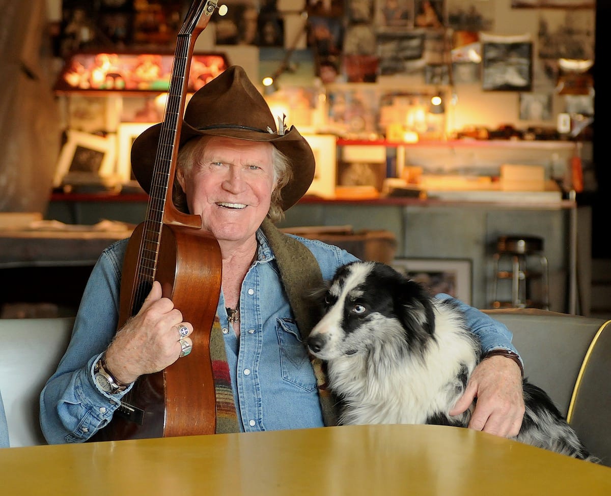 Billy Joe Shaver seated with his acoustic guitar and a black and white dog