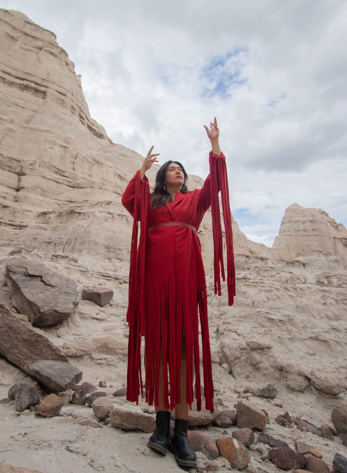 Black Belt Eagle Scout in red dress against a rocky backdrop, arms raised.