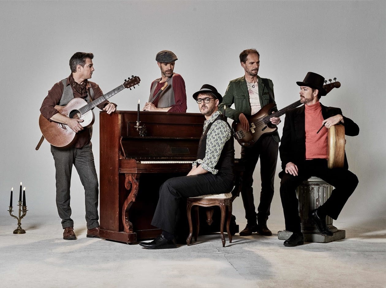 The five members of Doolin' gathered around a piano with various instruments