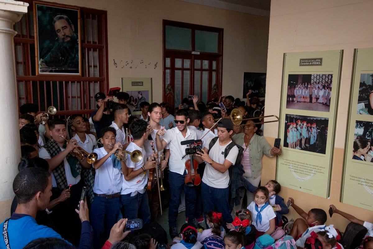 Students with instruments jam into a small space under a photo of Fidel Castro
