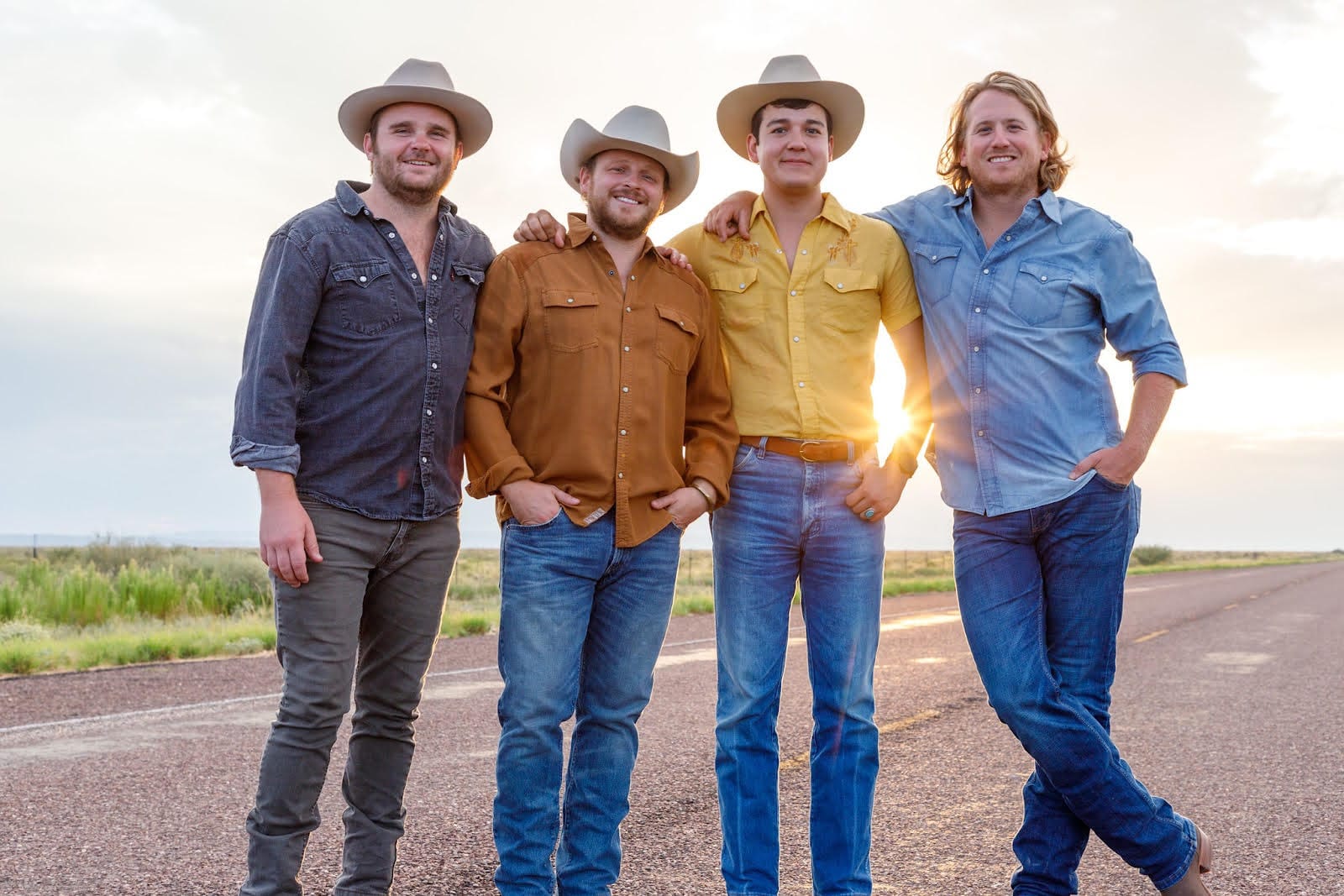 The four members of The Panhandlers stand on a road at sunset.