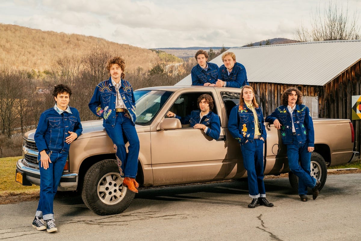 The Nude Party in matching blue jumpsuits around a tan pickup truck