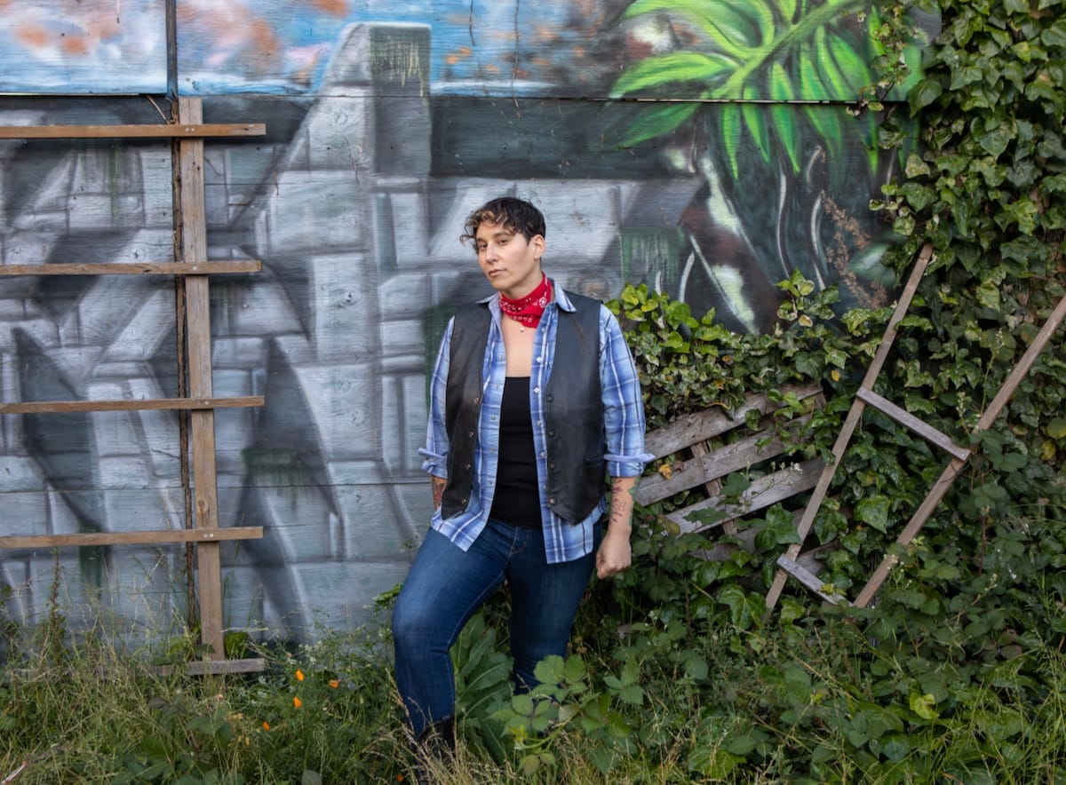 Mya Byrne against a painted wall with green foliage at her feet