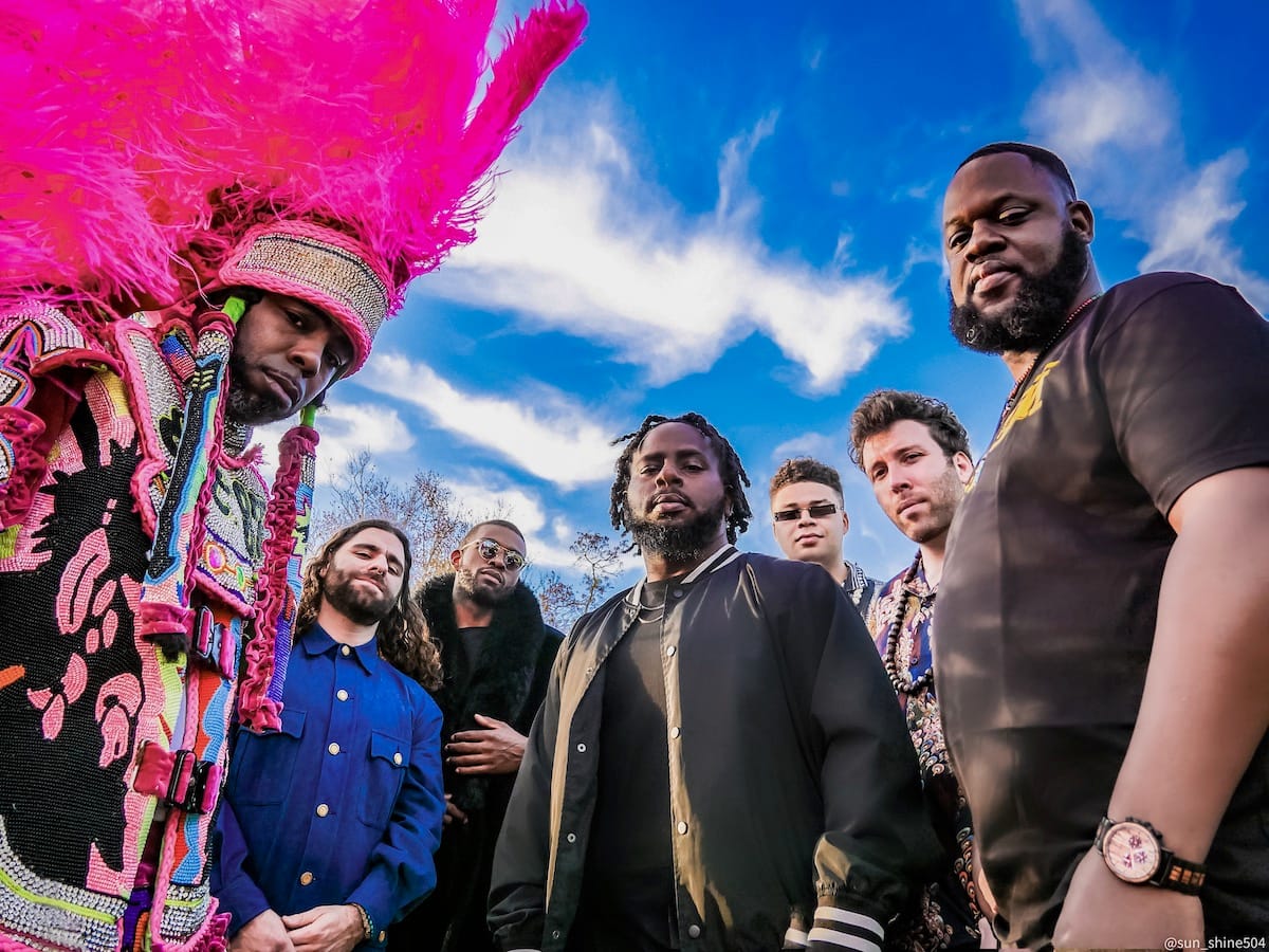 The seven members of The Rumble against a blue sky with wispy white clouds
