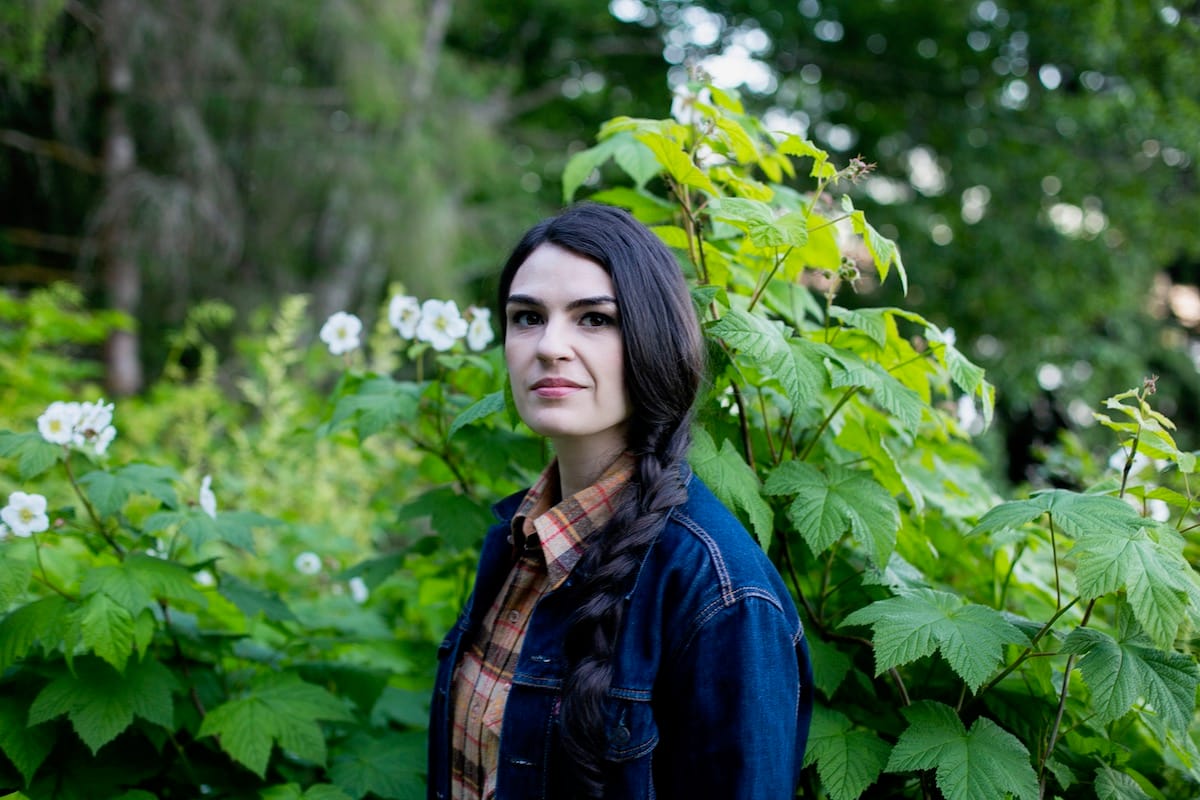 Annie Bartholomew on a beach holding a banjo
