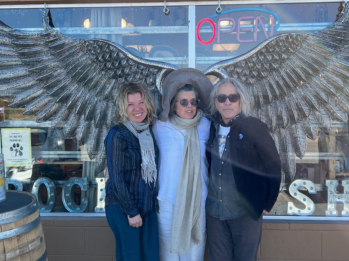 Three people stand in front of a metal sculpture of a set of wings