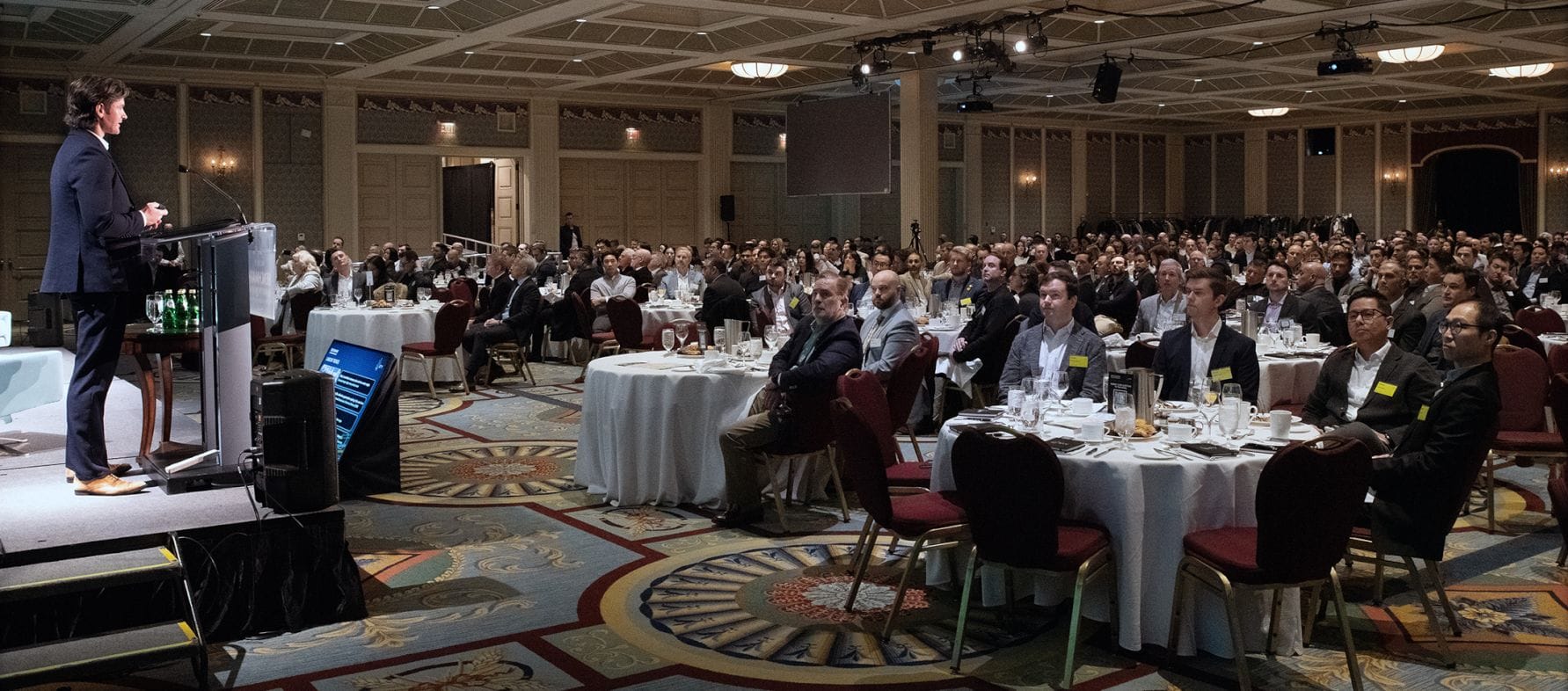 BTY representative on stage with podium in front of a ballroom full of people seated at round dinner tables.