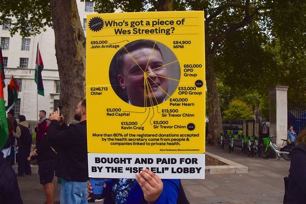 A protester holds a sign with alleged financial links to Wes
