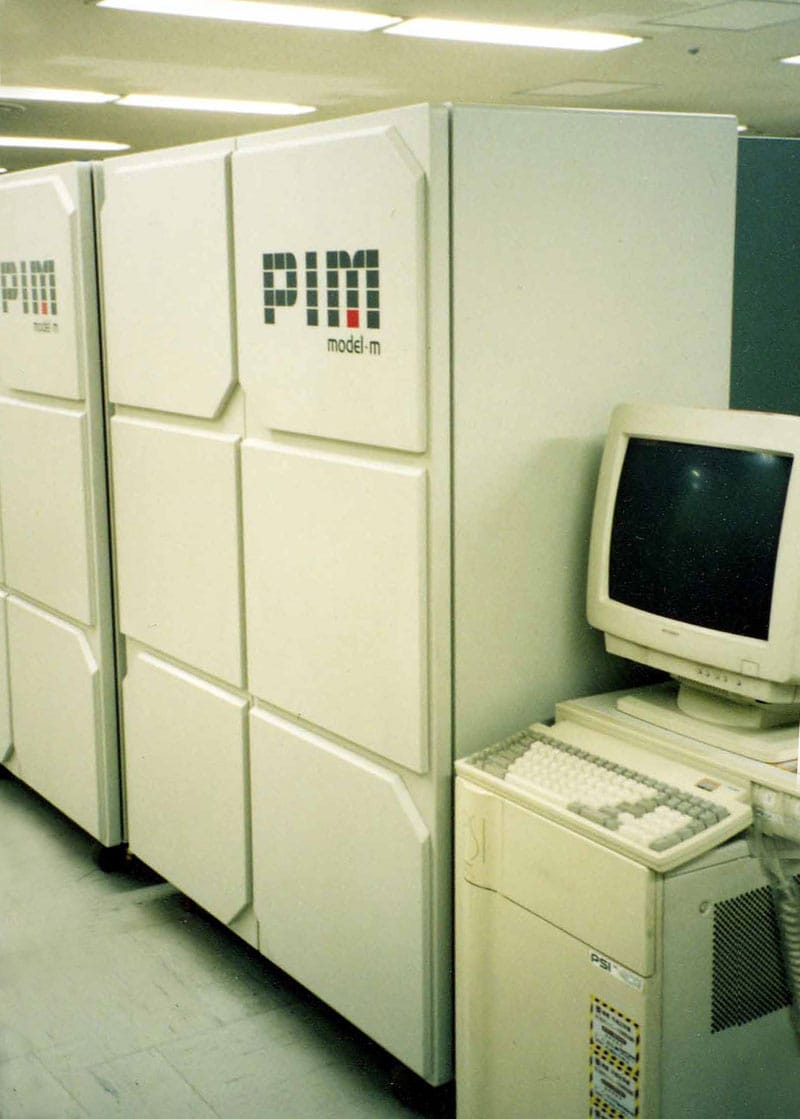 A photograph of a large, cabinet-style parallel computer system labeled “PIM model m,” shown as a row of tall white processor cabinets alongside a beige workstation with a CRT monitor and keyboard, emphasizing the scale and physical form of late-1980s high-performance computing hardware.