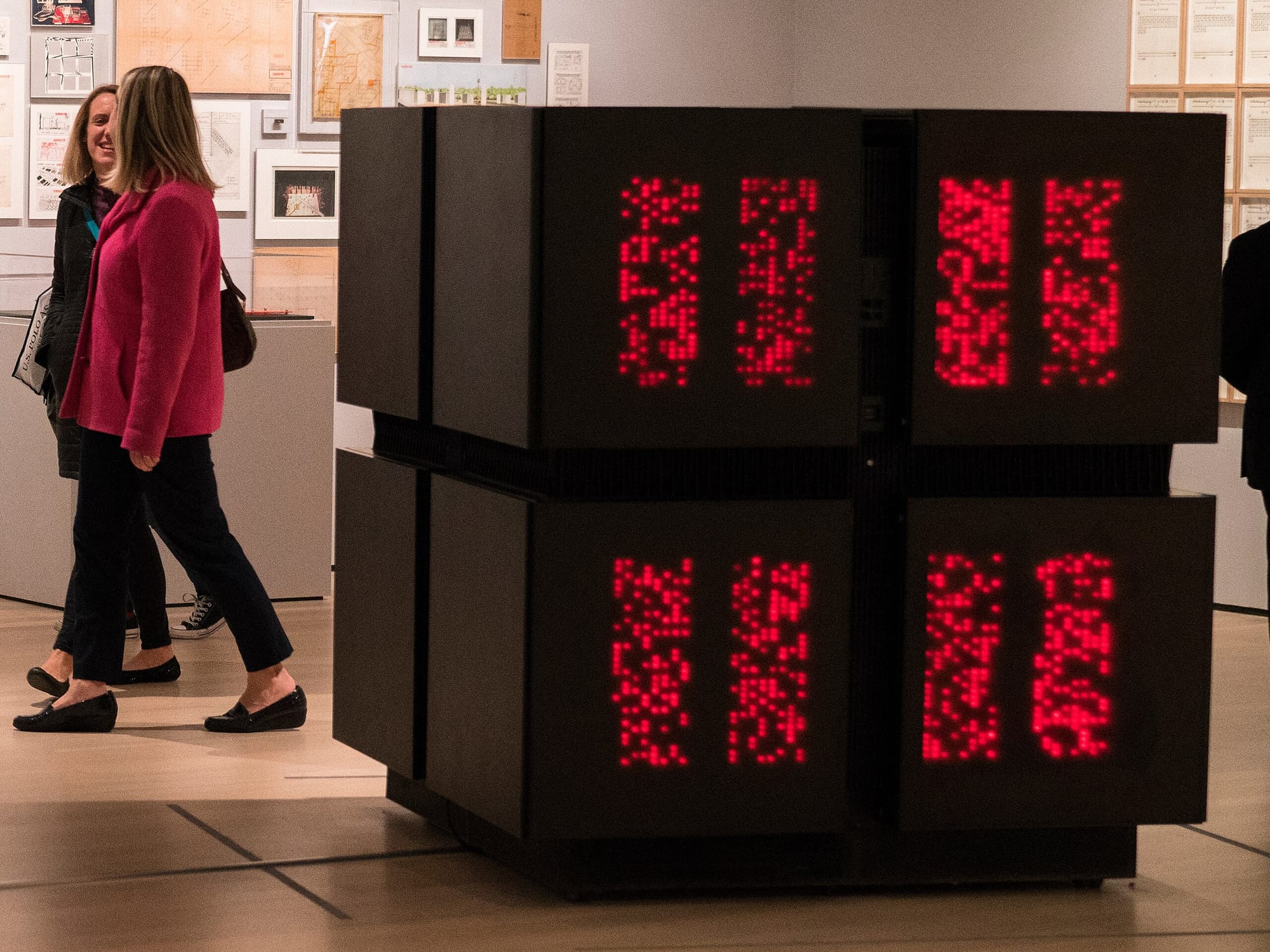 A museum gallery scene featuring a Connection Machine supercomputer, a large black cube with large panels of grid-aligned red LEDs glowing across its face, while visitors walk past, emphasizing the scale and just downright cool-as-hell design of early parallel computing hardware.