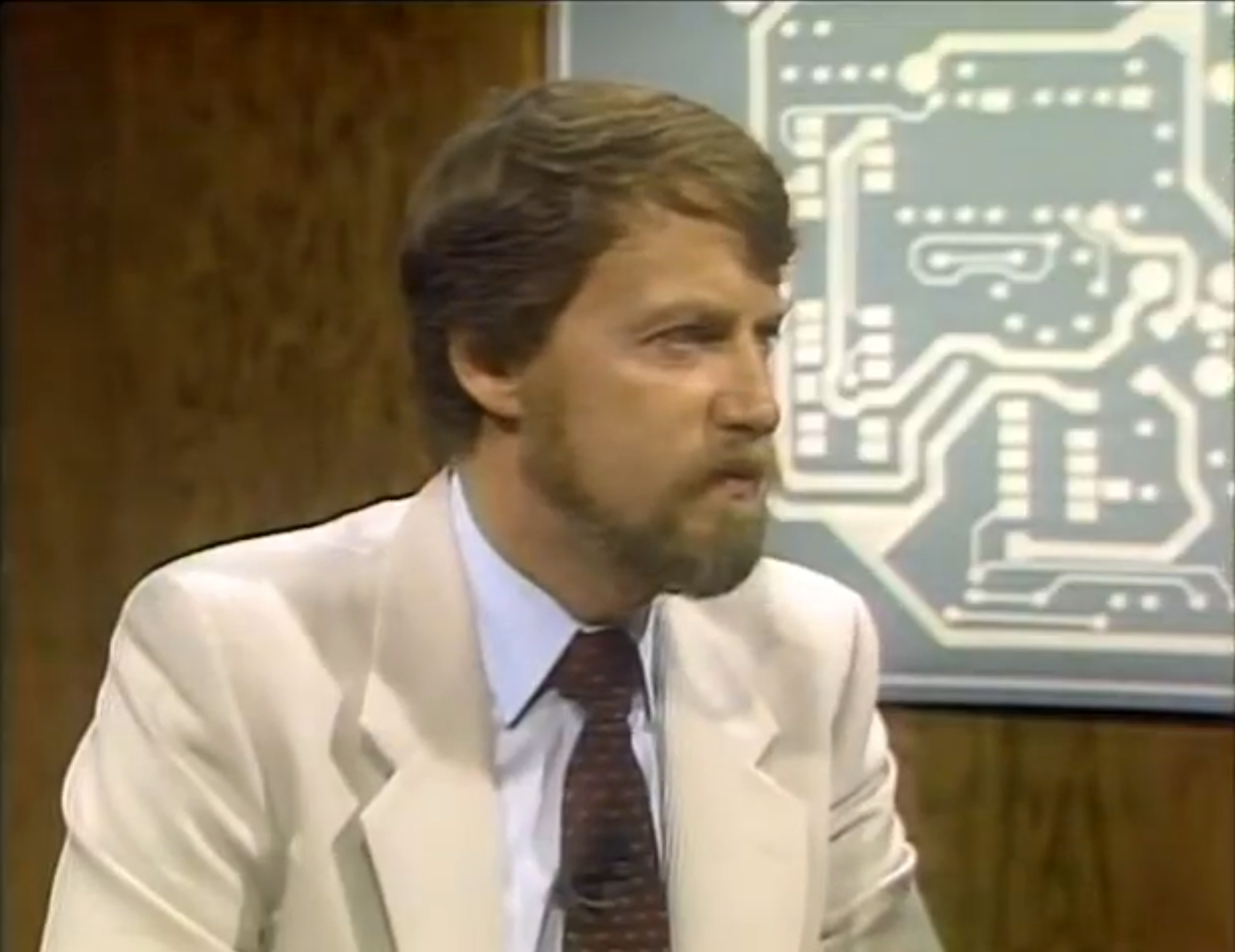 Screenshot from Computer Chronicles. Gary Kildall in a tan suit and brown patterned tie, face tight, lips pursed in skepticism.