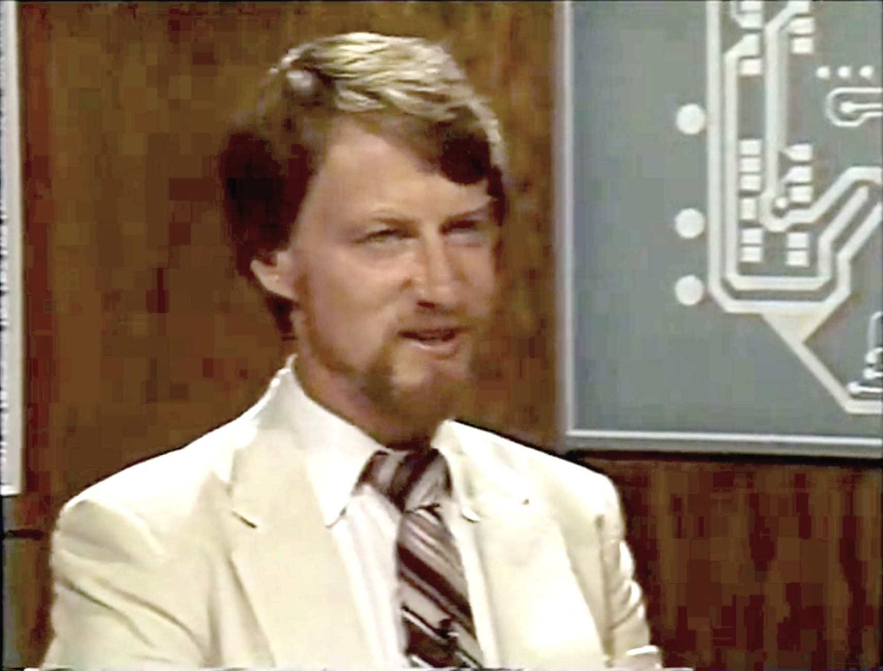 Screenshot from Computer Chronicles. Gary Kildall in a tan suit and brown striped tie, smiling, enjoying the conversation.