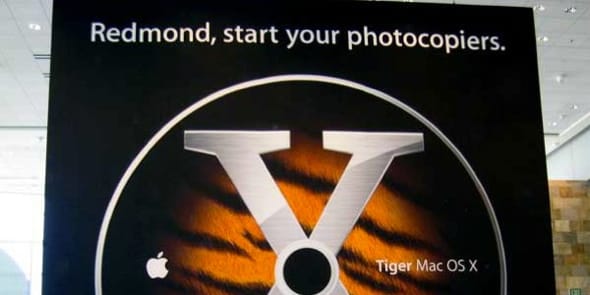 Banner image from an old WWDC when Mac OS X Tiger was announced. A giant image of the DVD-ROM fills a black background. The headline at the top says, "Redmond, start your photocopiers."