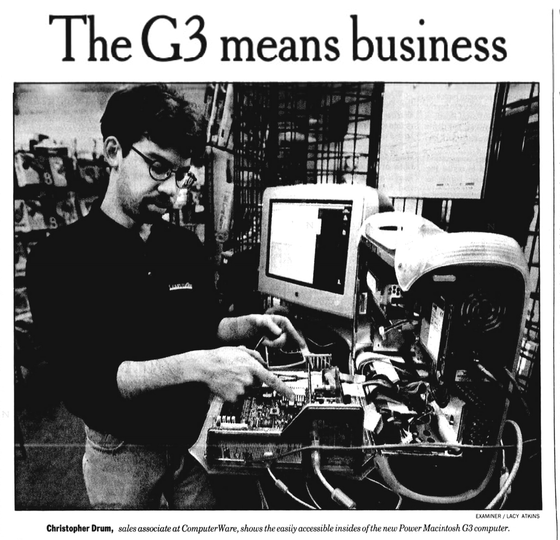 Snippet from the San Francisco Examiner. The headline reads, "The G3 means business" A large black and white photo of a much younger, thinner, bespectacled, goateed (my god, I'd forgotten that phase of my facial hair) me, pointing at features of the motherboard of the G3. The caption reads, "Christopher Drum, sales associate at ComputerWare, shows the easily accessible insides of the new Power Macintosh G3 computer." Photo for the Examiner by Lacy Atkins.