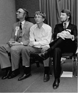 Photo of Bill Gates sitting next to Gary Kildall. Gates is tense, coiled, leaning forward, arms crossed. Kildall is sitting back, legs crossed, hands clasped, smiling pleasantly.