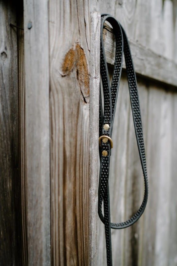 An empty black leash hanging on a weathered wood fence