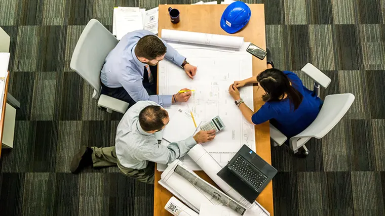 Photo of three people sitting around a table looking at a blueprint.