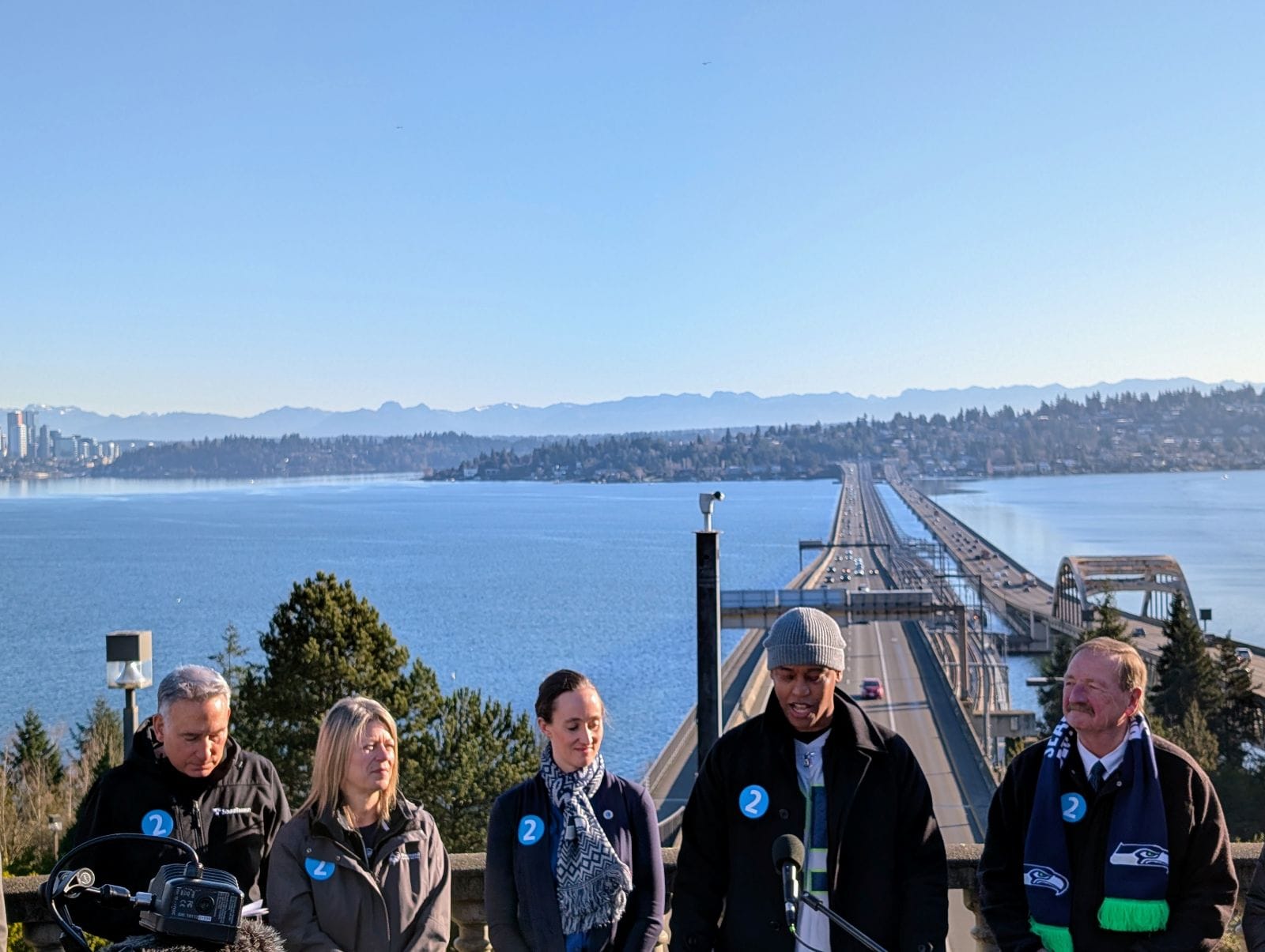 Lake Washington, the I-90 floating bridge, and Bellevue skyline is right over their shoulders as Sound Transit leaders make their announcement at I-90 Portal Park in Seattle.