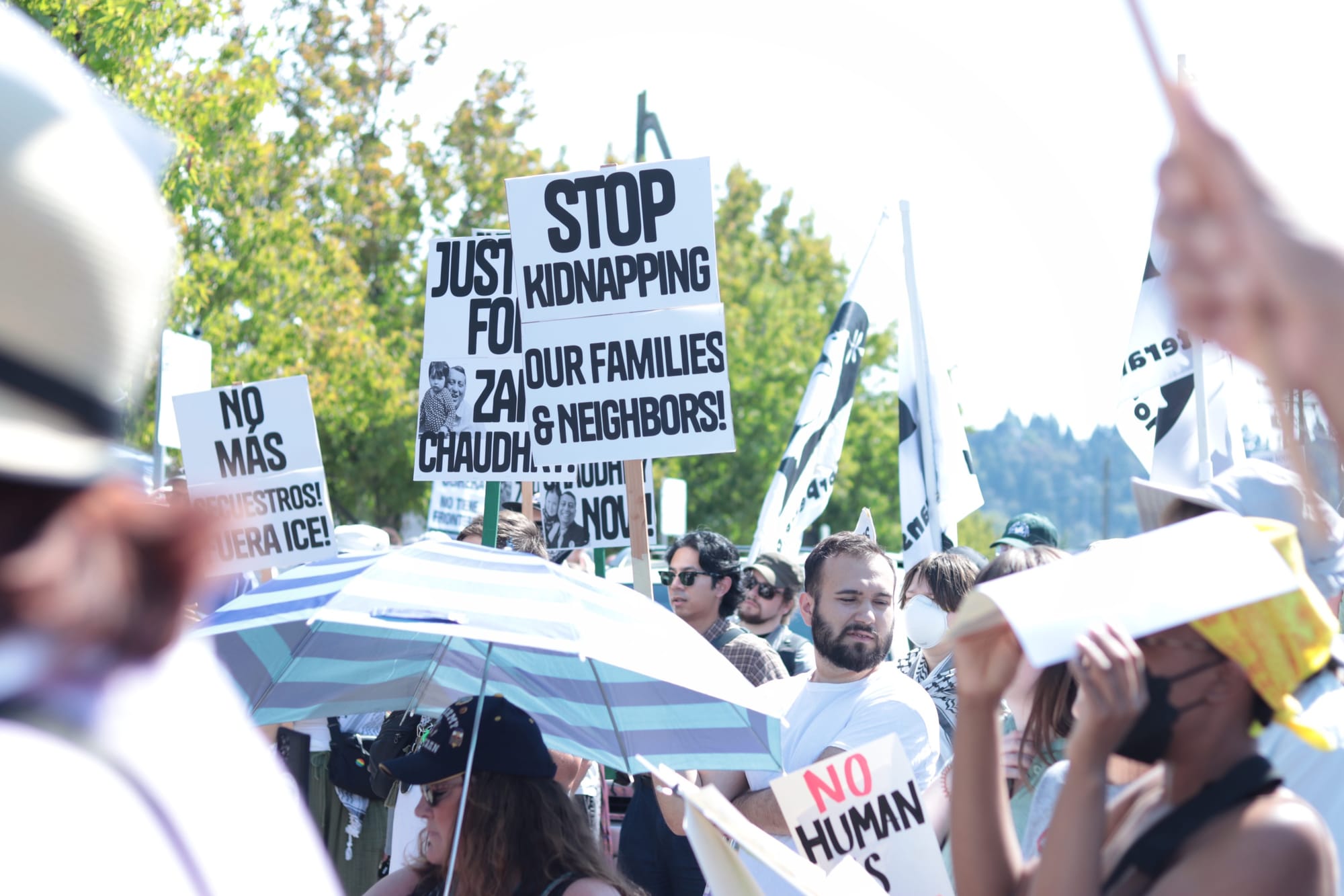 A crowd of protesters holds signs like slogans such as "Stop Kidnapping our families and neighbors!" and "No más secuestros. Fuera ICE!"