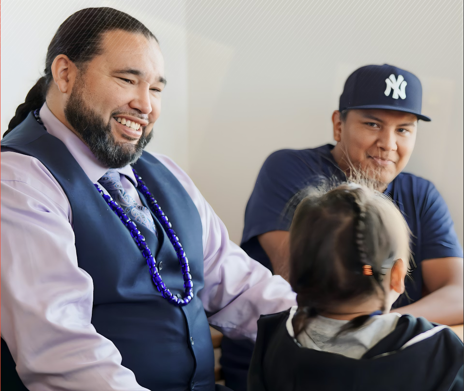 DePoe where a purple dress shirt and vest with a necklace and talks to two young people, smiling.