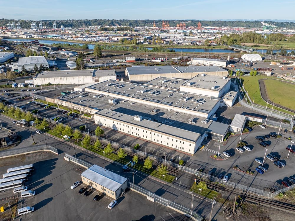 An aerial drone image of the sprawling detention center with the tower cranes of the Port of Tacoma in the background
