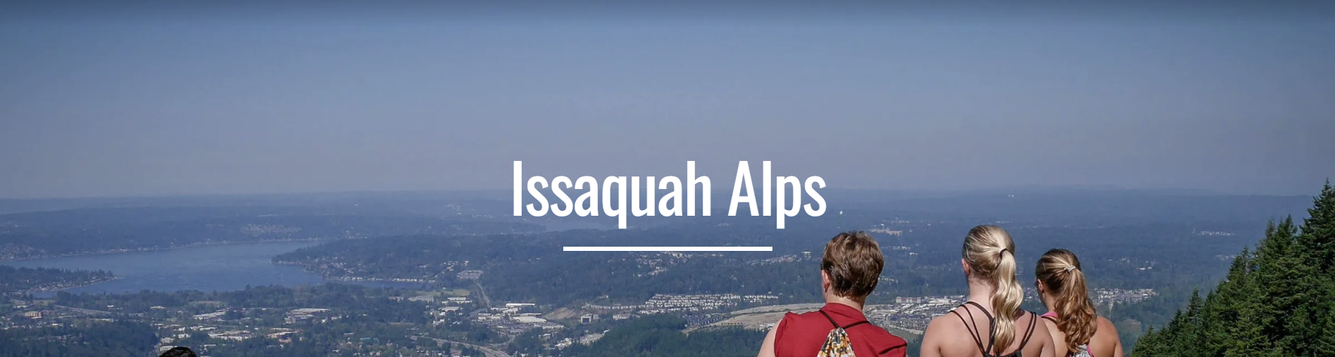 Three hikers stand atop a peak in the Issaquah Alps looking down on the cities below.
