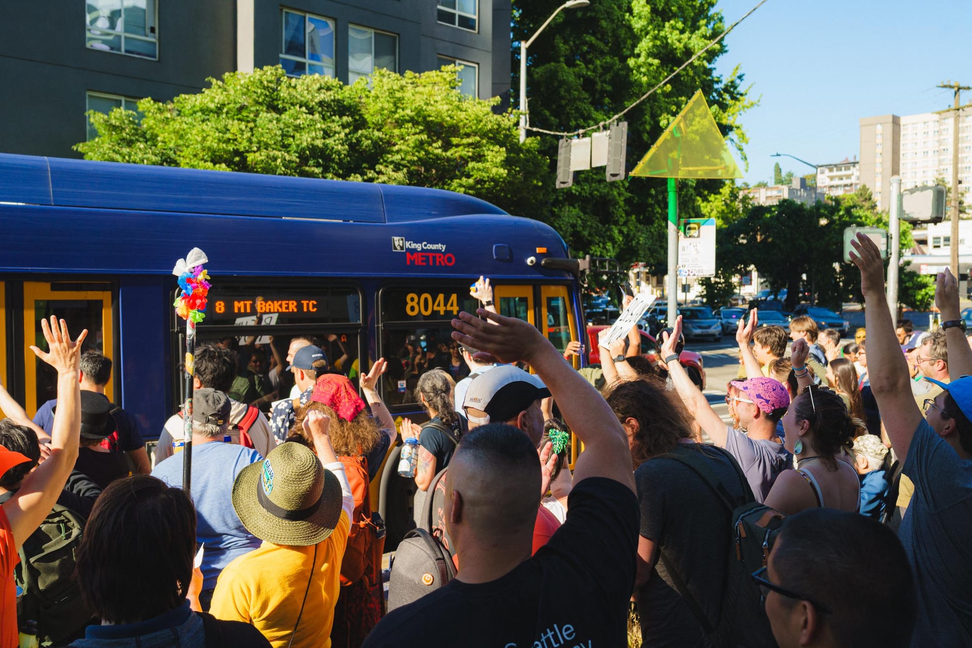 A group of nearly a 100 advocates wait at the end of the route where they raced Route 8 and won, even as they danced, hopscotched, unicycled and so forth. They wave at the bus as it shows up at a stop on a congested Denny Way.