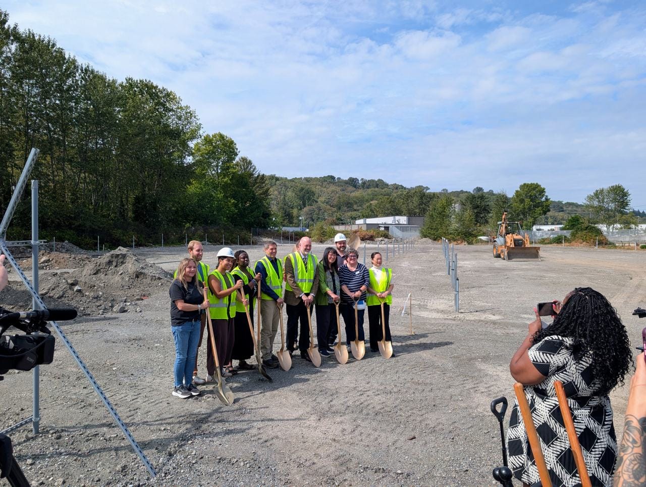 10 officials pose with golden shovels at a groundbreaking ceremony in a gravel lot that will host the RV safe lot and tiny house village.