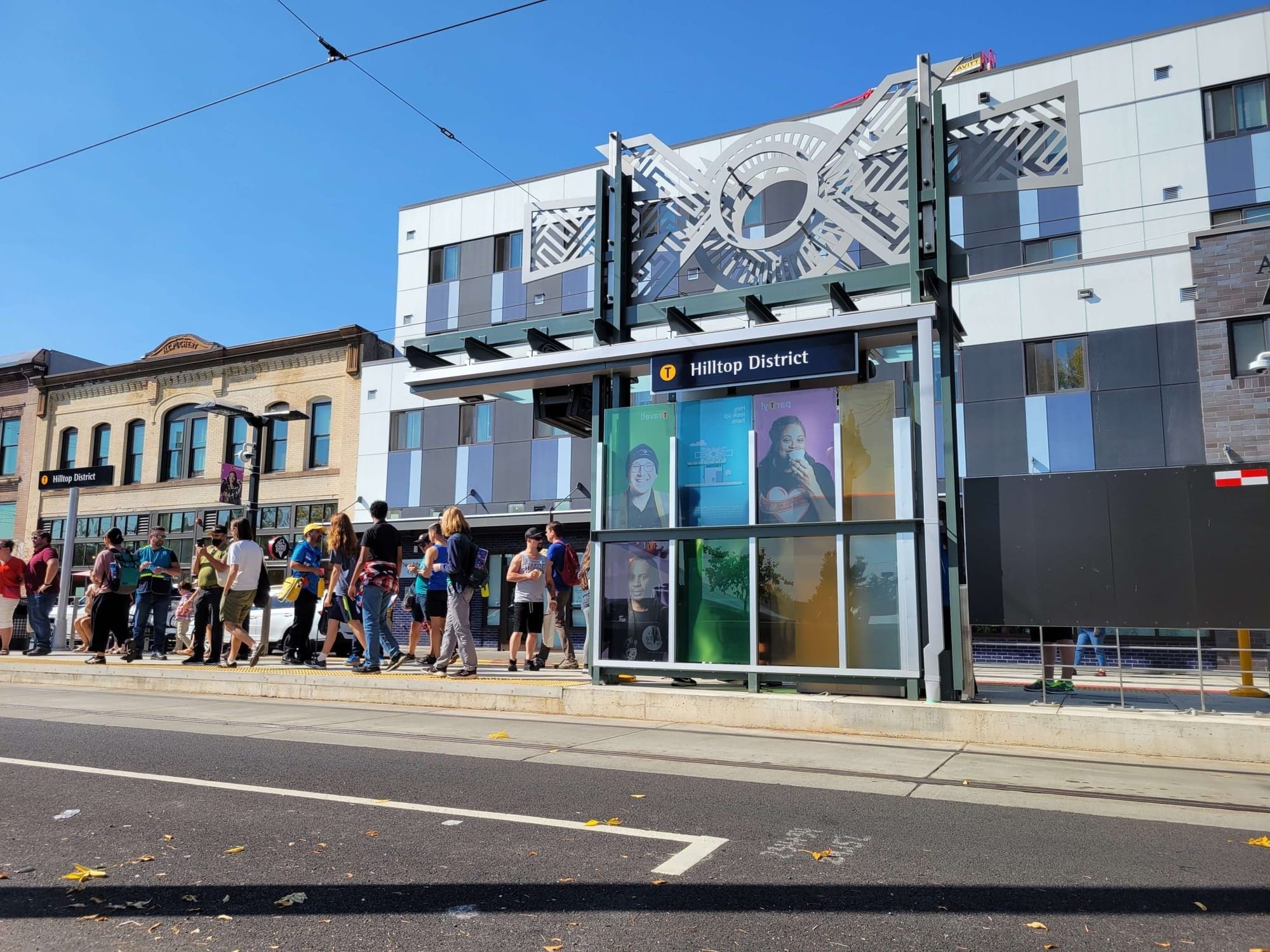 Sunny day with a crowd of people waiting for the streetcar to arrive.