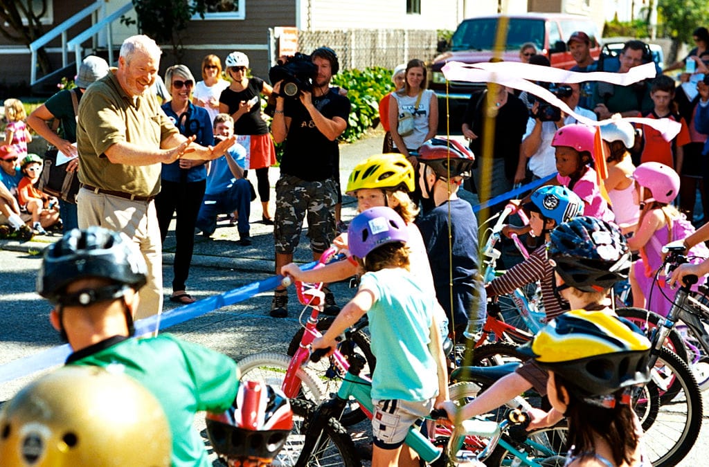Mayor Mike McGinn cutting the ribbon on the Ballard Neighborhood Greenway as kids on bikes line up to get a first ride. (Credit: Dennis Bratland)