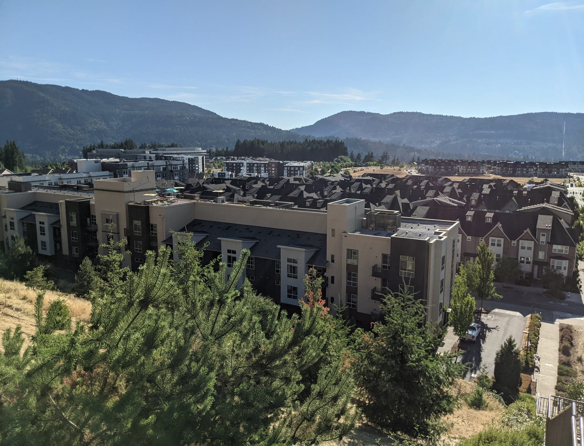 A grouping of low-rise apartments and townhomes with trees and Issaquah foothills in the background.