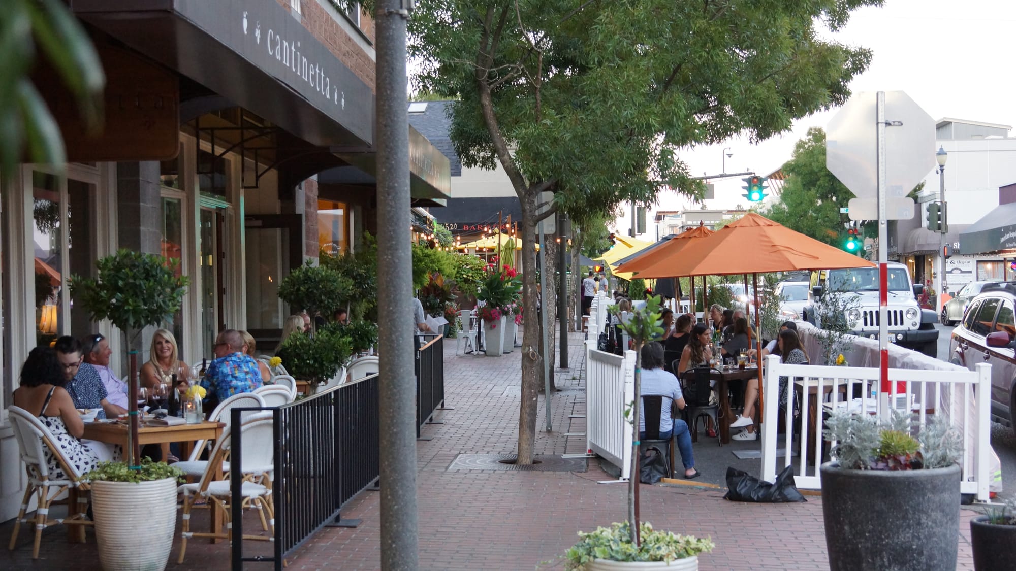 A photo of an outdoor café with sidewalk terrace divided in two parts. The first is next to the building and the second is next to the street.
